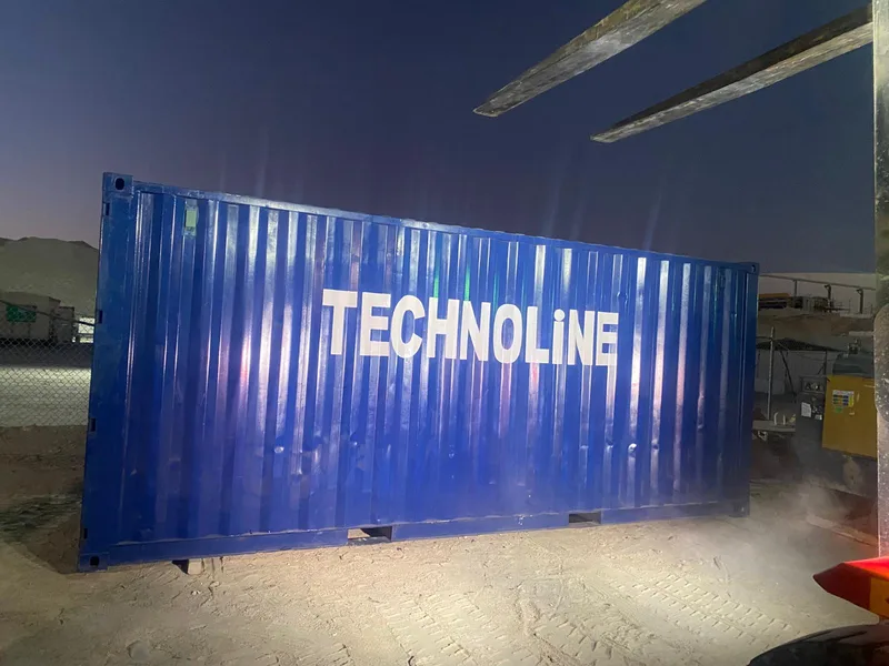 Blue Technoline container being positioned at a site by forklift at dusk