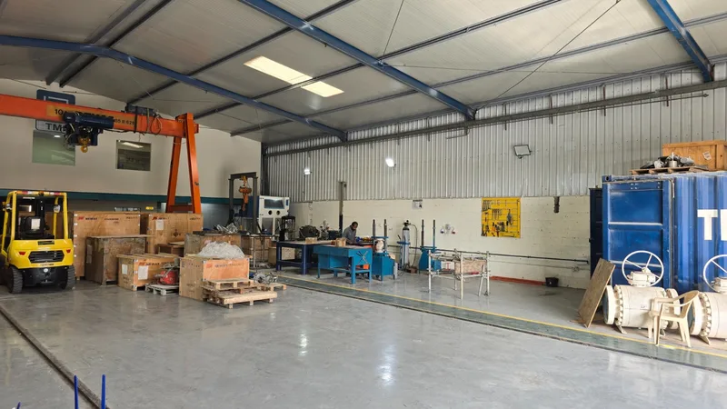 Workshop floor with a gantry crane, forklift, repair benches, crated valves and large ball valves